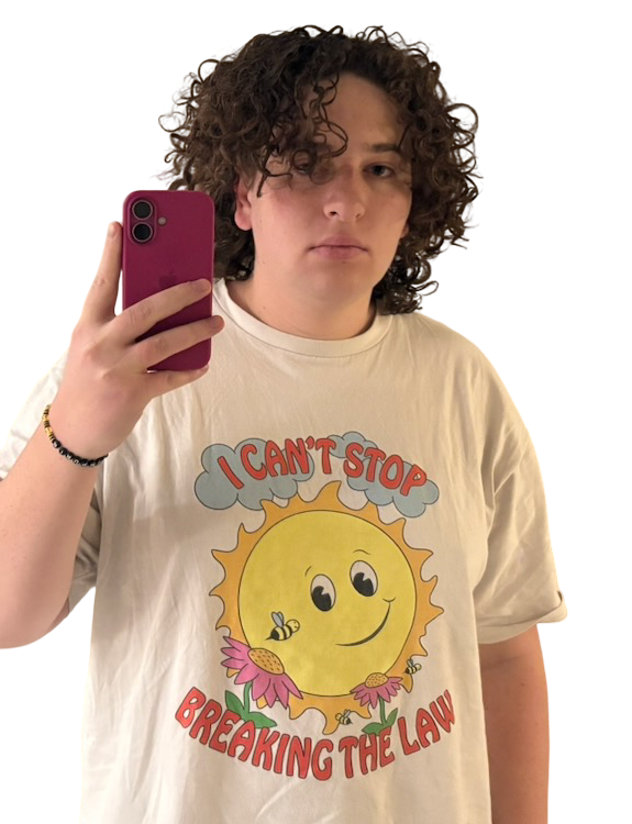 A photo of Cass staring blankly. She is wearing a wrinkled, oversized white T-shirt with clip art of a smiling sun and flowers with the text "I can't stop breaking the law".